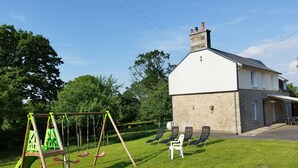 A house with a stone exterior, a white roof, and a chimney. In front, there is a swing set and several lawn chairs.