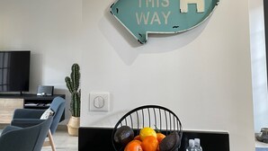A kitchen area with a teal sign reading "BEACH THIS WAY" on the wall, a black countertop, a fruit bowl with oranges and a lemon, and a television on a stand. - 2 bedrooms, 2 bathrooms appartement with terrace and balcony, close to beaches (Arcachon)