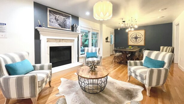 A living room with striped armchairs, a fireplace, a dining area, and a chandelier.