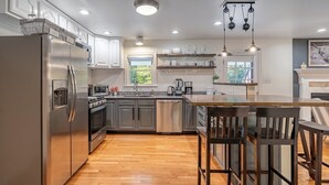 A modern kitchen with stainless steel appliances, wooden flooring, and pendant lighting.