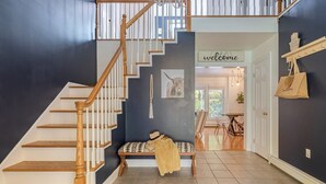 A staircase with wooden railings and a bench with a patterned cushion in a hallway with dark walls and tiled flooring.