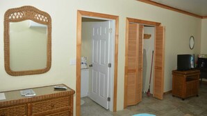 A room with a large mirror, a television, a wicker dresser, and a door leading to another room. - Cassaruina Studio 3 (Rolleville)
