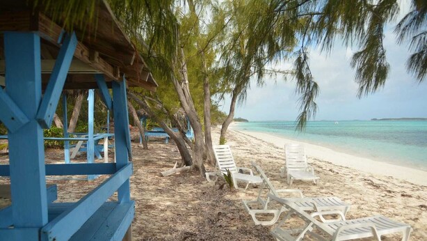 A beach with white lounge chairs and a blue structure. - Cassaruina Studio 3 (Rolleville)