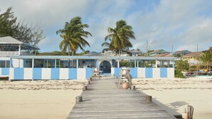 A beachside pier leading to a building with a blue and white facade, palm trees, and beach houses in the background. - Cassaruina Studio 3 (Rolleville)