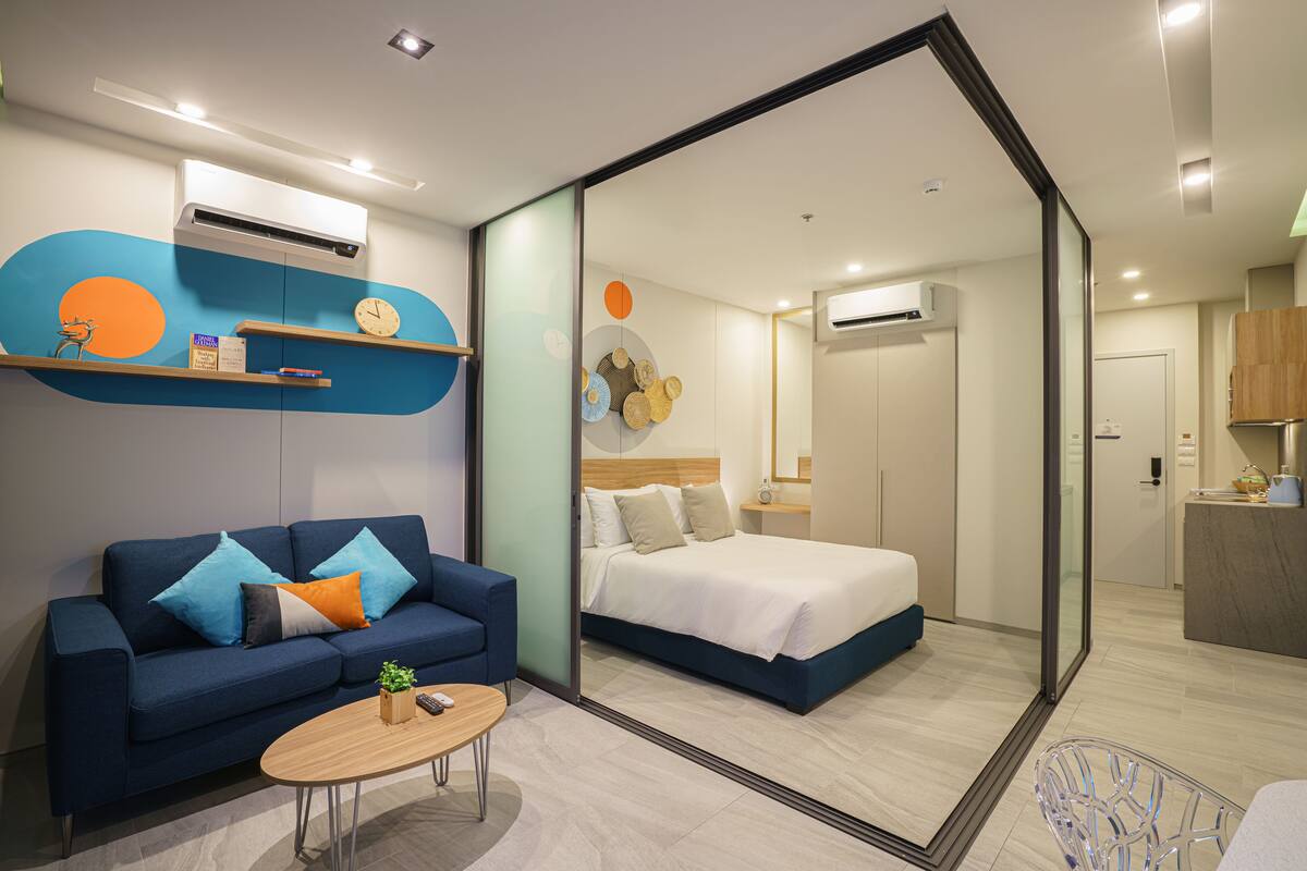 Una habitación de hotel moderna con sofá, cama, mesa de centro y un baño visible a través de una pared de vidrio.