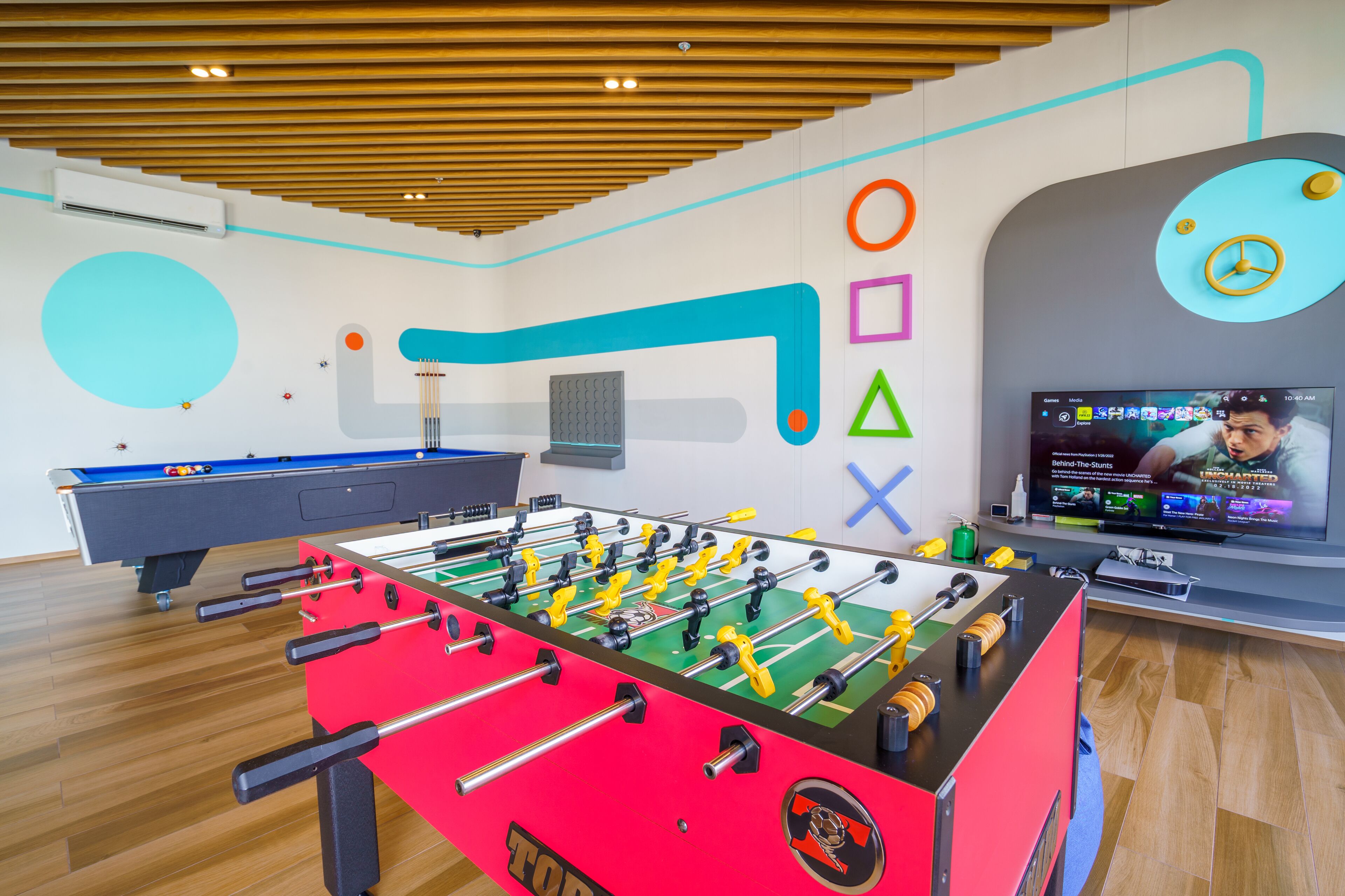 Una habitación con mesa de futbolín, mesa de billar y un televisor mostrando un programa deportivo.