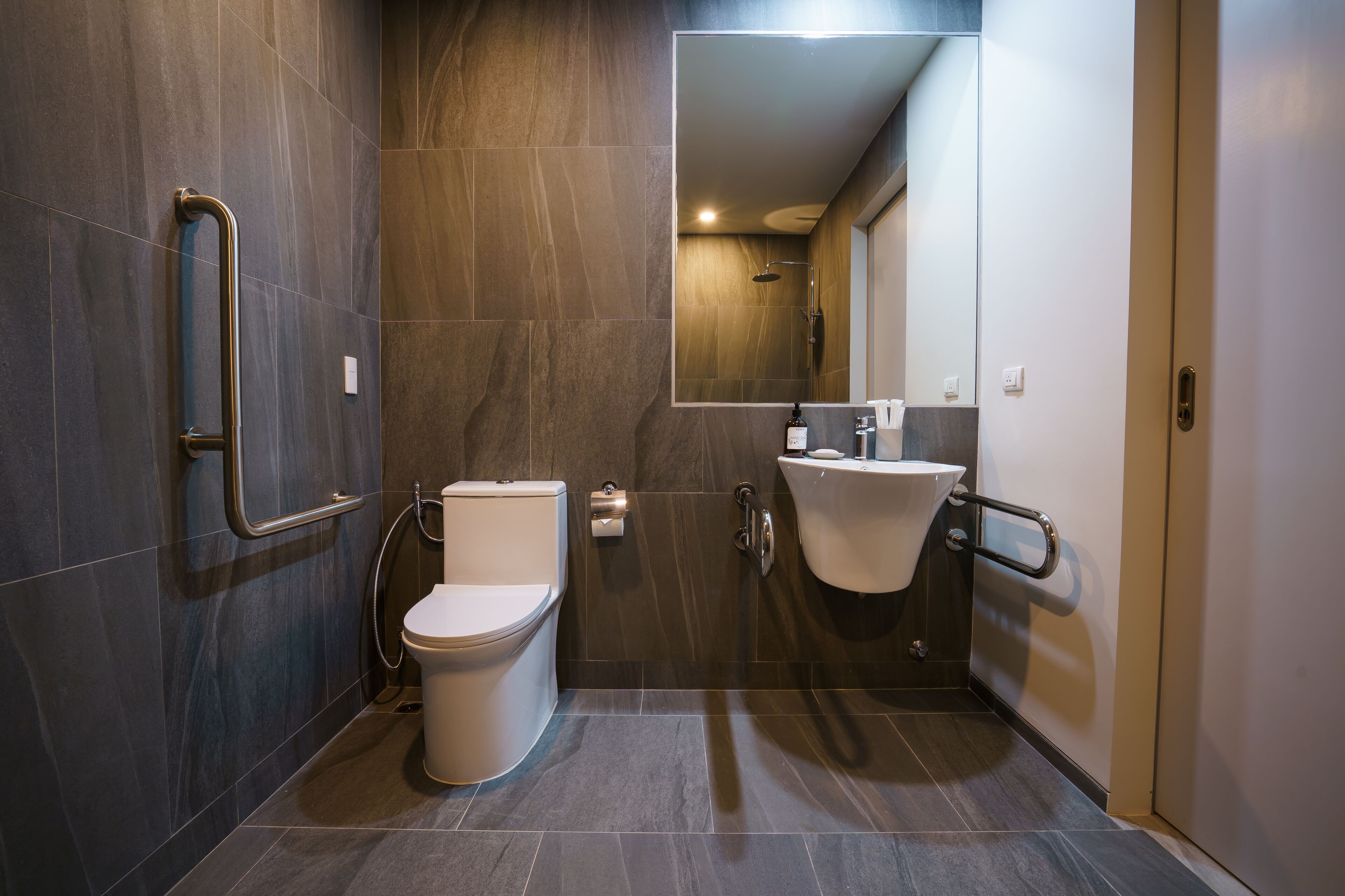 Un baño moderno con inodoro, bidé y lavamanos, equipado con barras de apoyo.