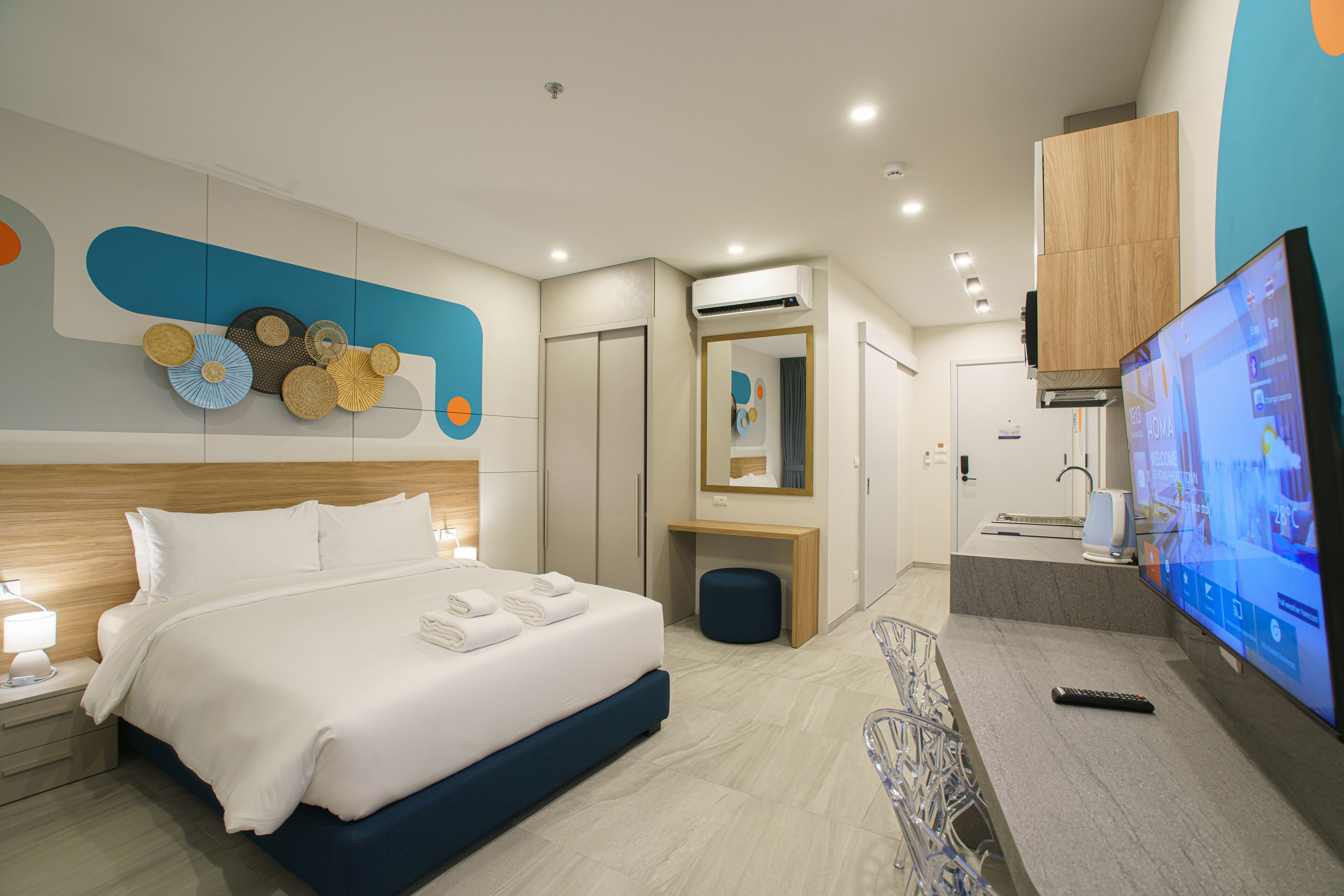 A modern hotel room with a large bed, a TV, a desk with a computer, and a bathroom with a mirror and sink.
