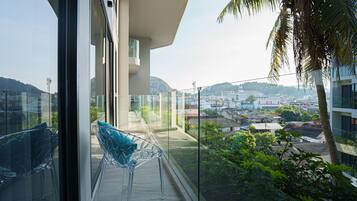 A balcony with clear glass railings, a clear plastic chair, and a view of a cityscape with buildings and hills in the distance.