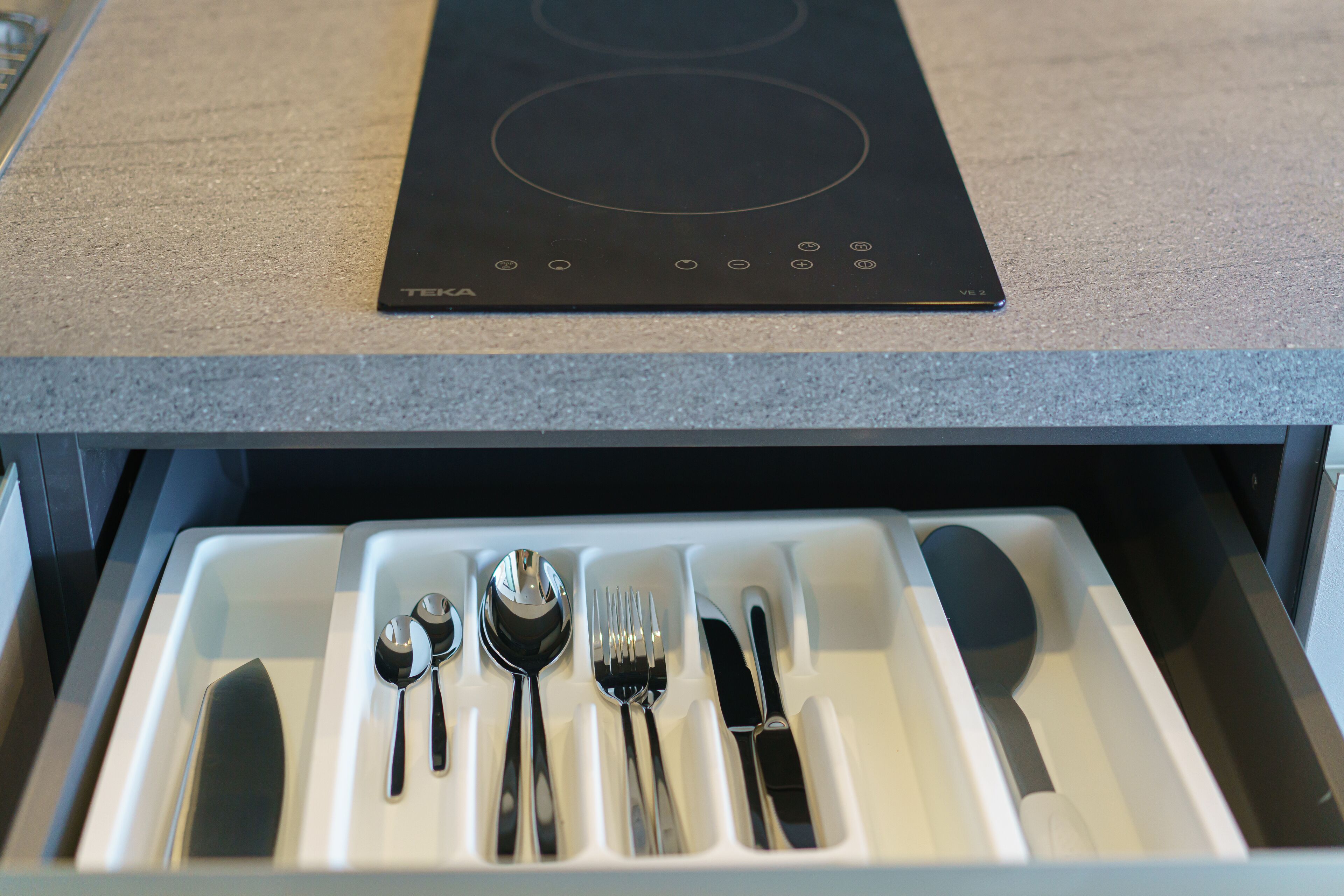 Une cuisine dotée d’une plaque de cuisson à induction noire et d’un tiroir contenant des ustensiles de cuisine.
