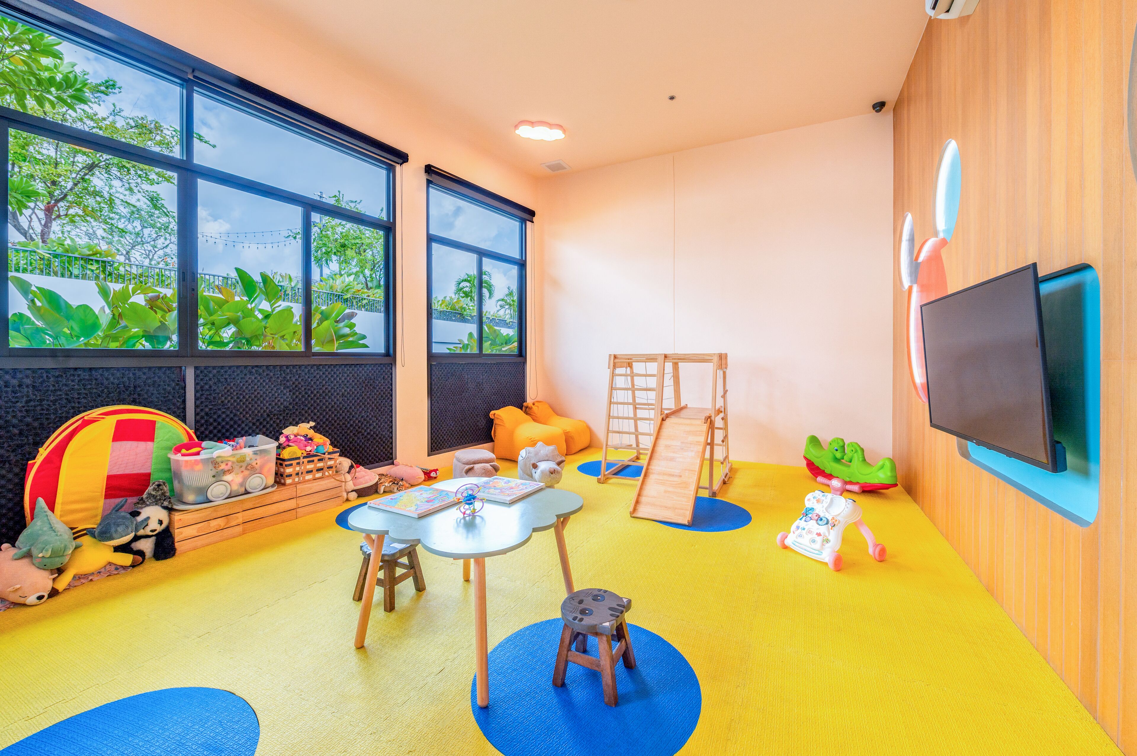 Een kinderkamer met een groot raam, een televisie en diverse speelgoed en speeltoestellen.