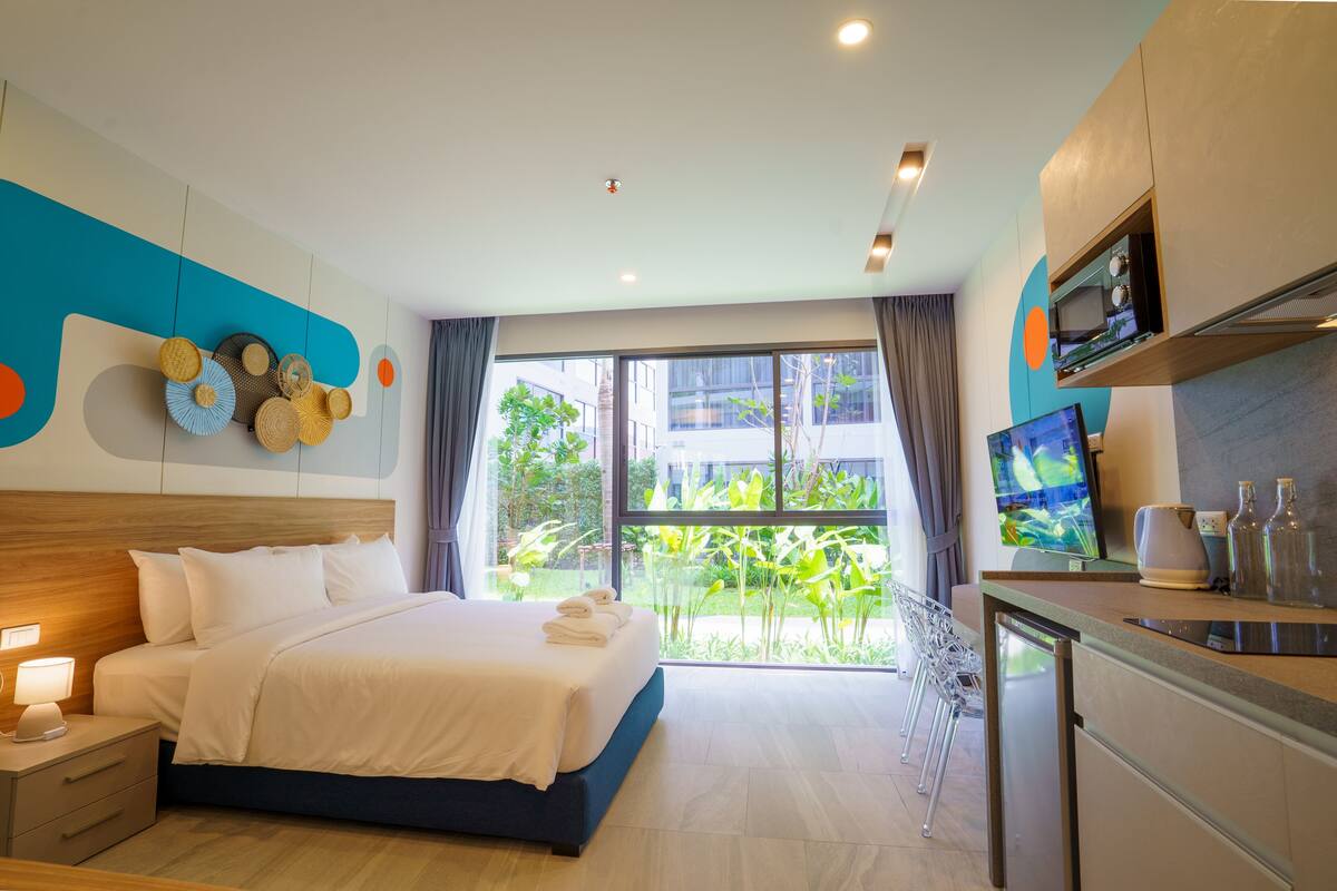 Una habitación de hotel moderna con una cama grande, un escritorio con televisor y vistas a zonas verdes.