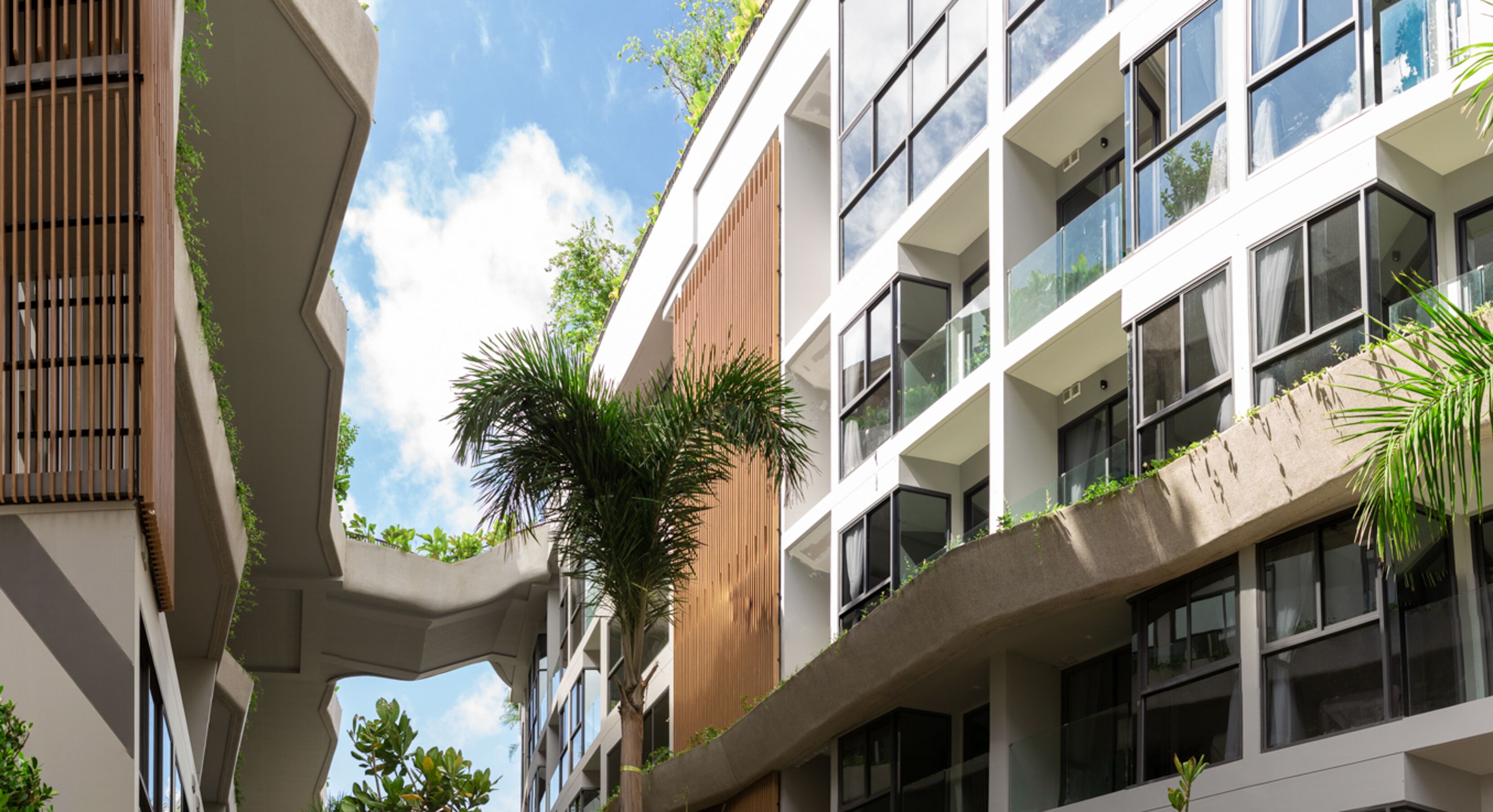 Een modern gebouw met balkons, grote ramen en wat groen.