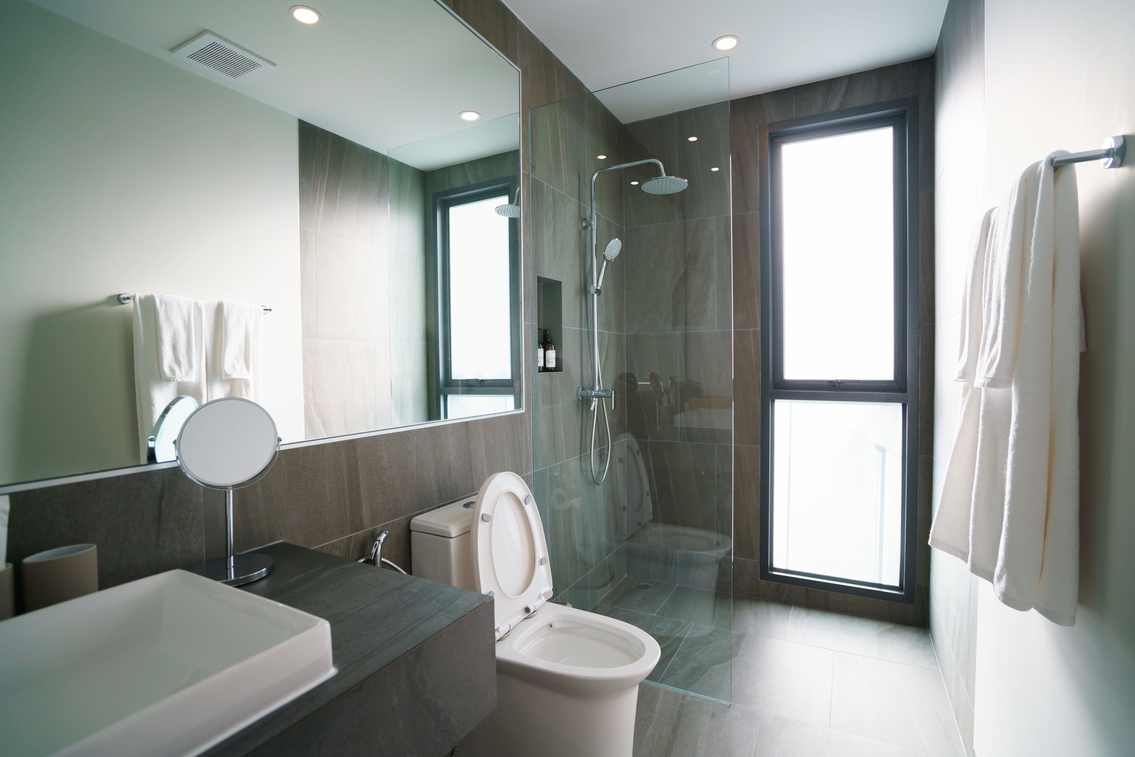 A modern bathroom with a glass-enclosed shower, a large mirror, and a toilet.