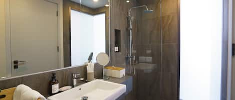 A modern bathroom with a large mirror, a white sink, and a glass-enclosed shower.