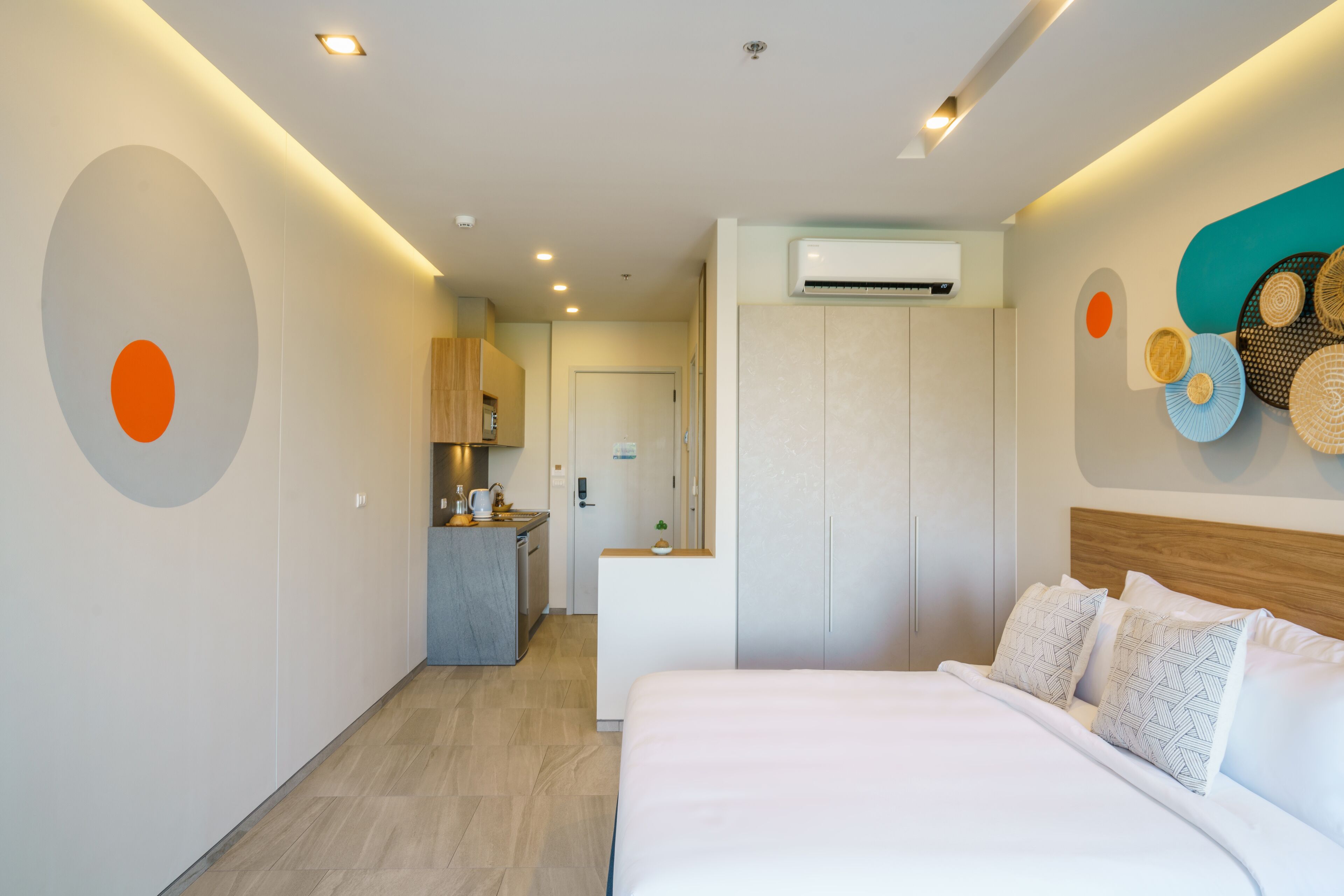 A modern hotel room with a bed, a desk, and a kitchenette.