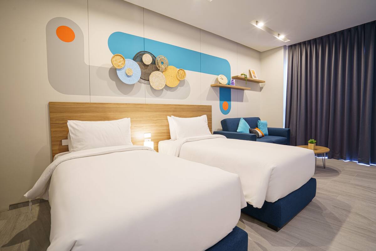 Habitación de hotel con dos camas, un sofá, una mesita y una pared decorada.