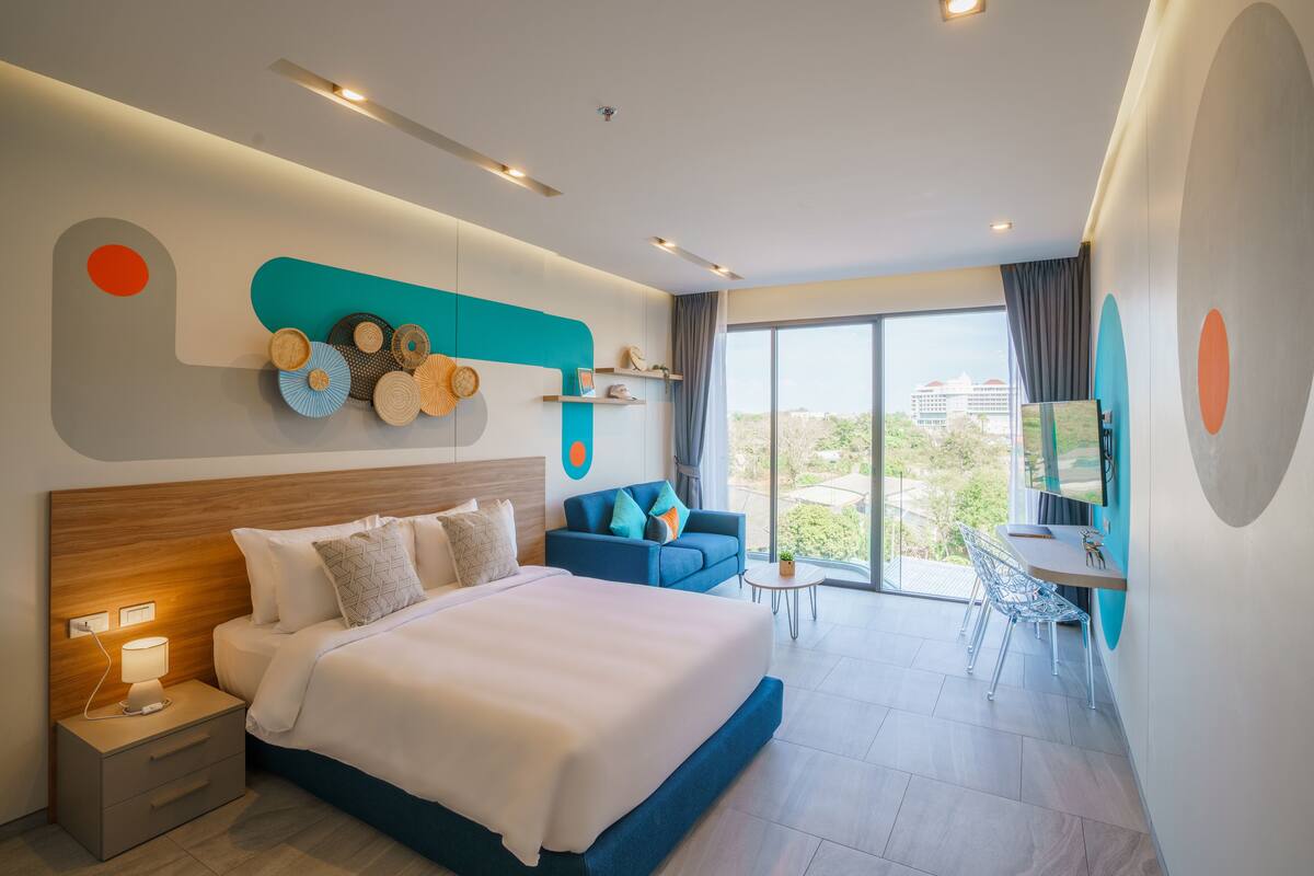 Una habitación de hotel moderna con una cama grande, un sofá, una mesita y un balcón con vistas.