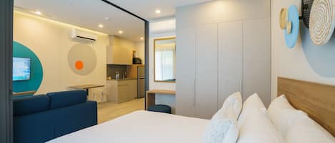 A modern hotel room with a large bed, a sofa, a kitchenette, and a bathroom.