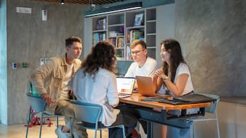 Un grupo de cuatro personas sentadas alrededor de una mesa en un ambiente interior moderno con estanterías al fondo.