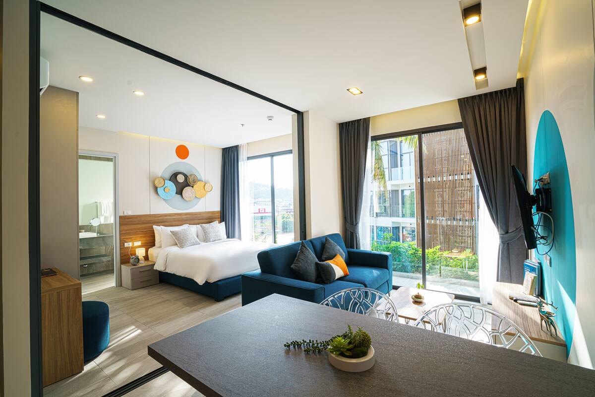 Una habitación de hotel moderna con cama, sofá, mesa de comedor y vistas al exterior.