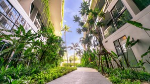 A pathway flanked by lush greenery and modern buildings with large windows and balconies. - HOMA Phuket Town (Ratsada)