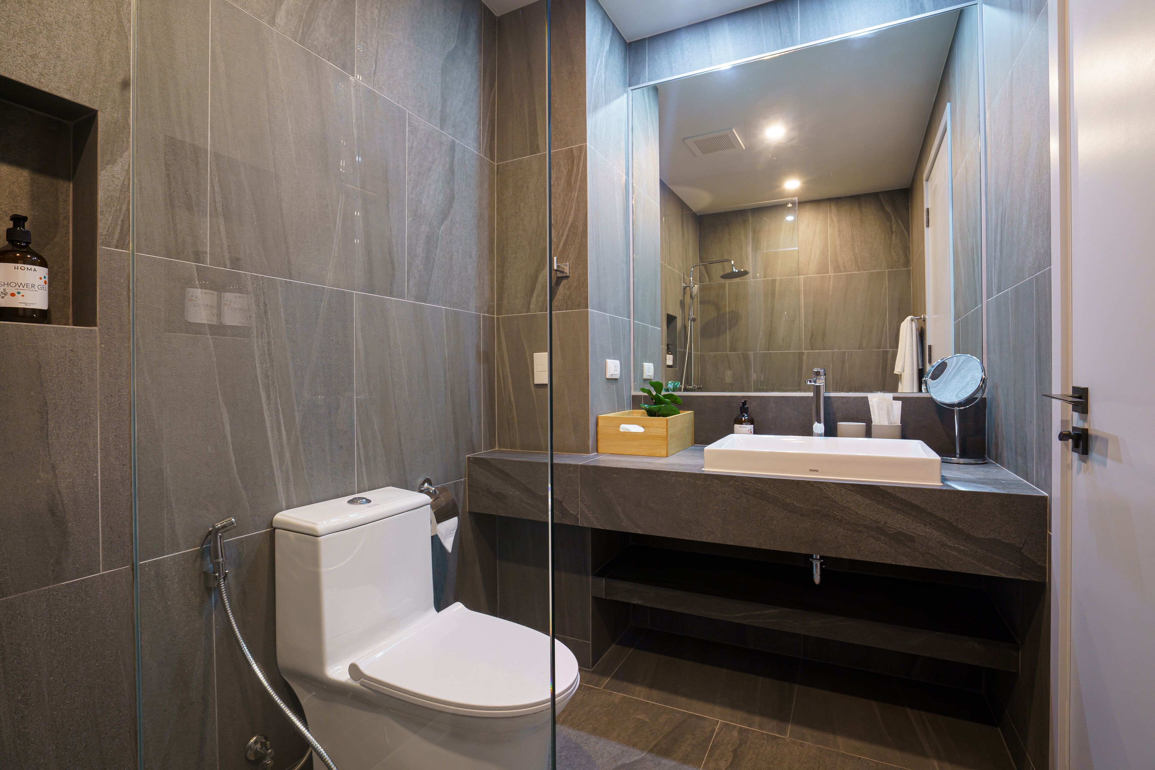 Un bagno moderno con doccia vetrata, un water bianco, uno specchio grande e una scatola di legno sul mobile lavabo.