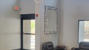 Ein geräumiges Zimmer mit Schachbrettmuster-Boden, zwei Ledersesseln, einem kleinen Tisch und einem dekorativen Spiegel an der Wand.