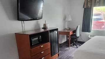 Une chambre d’hôtel équipée d’un lit, d’un bureau, d’une chaise, d’un téléviseur fixé au mur et d’une fenêtre avec des rideaux.