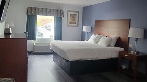 Ein Hotelzimmer mit Bett, Nachttischen, Schreibtisch, Stuhl, Fernseher und einem Fenster mit Vorhängen.