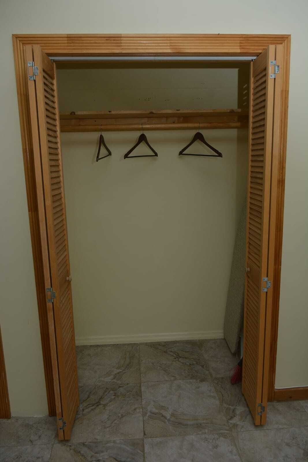 Ein Holzkleiderkasten mit Schiebetür, ein Marmorboden und drei schwarze Kleiderbügel im Inneren.