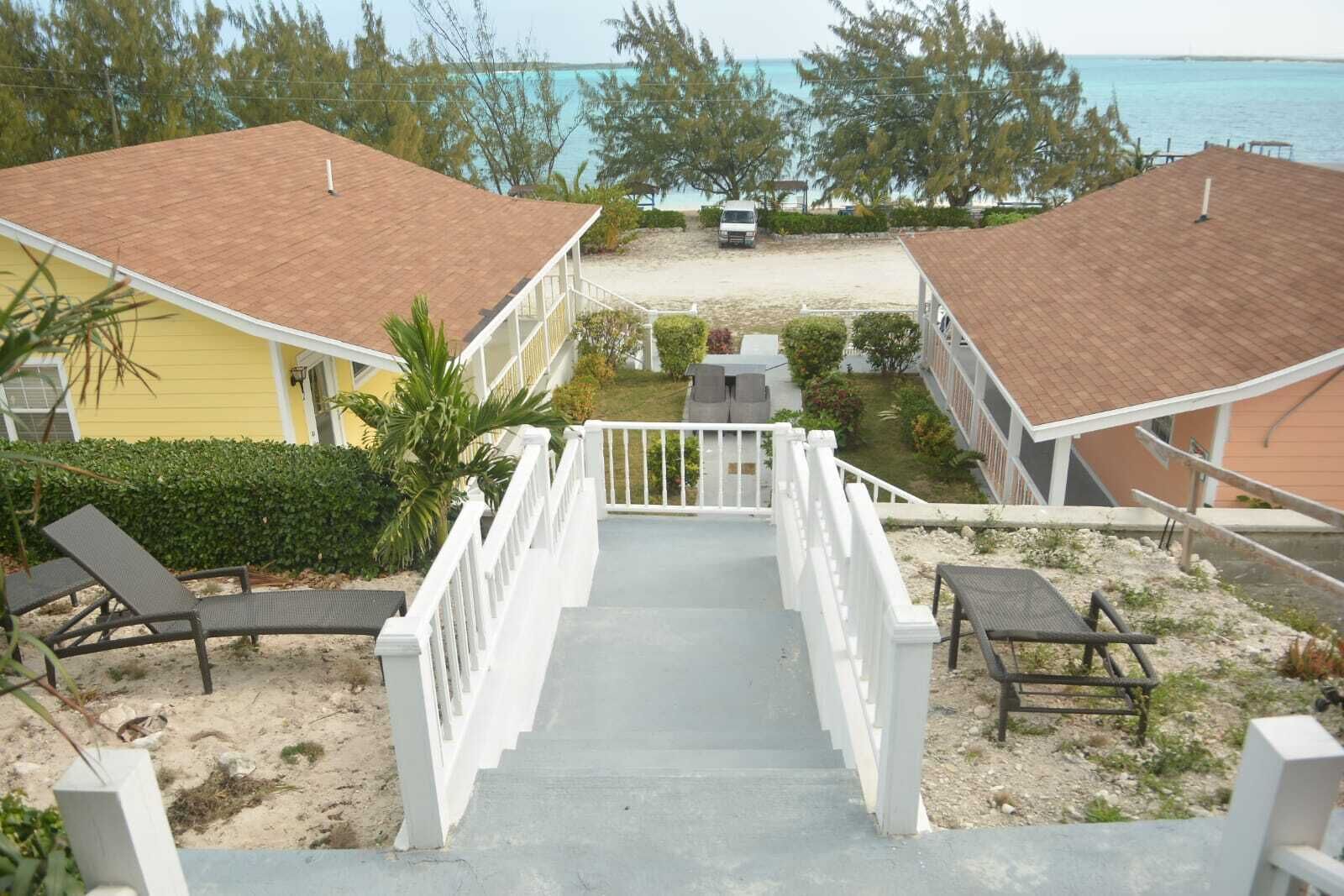 A beachfront property with a staircase leading to a covered area, lounge chairs, and a view of the ocean.