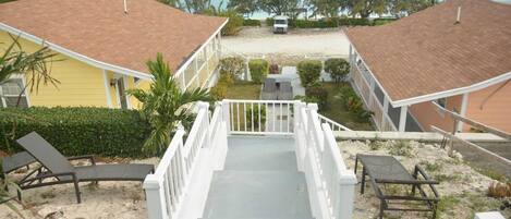 A beachfront property with a staircase leading to a covered area, lounge chairs, and a view of the ocean.