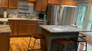 A modern kitchen with wooden cabinets, a stainless steel refrigerator, and a bar area with stools. - Beautiful lake house perfect for amazing getaways! (Fair Play)