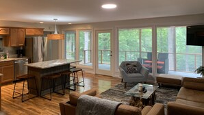A modern kitchen with a central island, wooden bar stools, and a dining area with a sofa and a coffee table. - Beautiful lake house perfect for amazing getaways! (Fair Play)