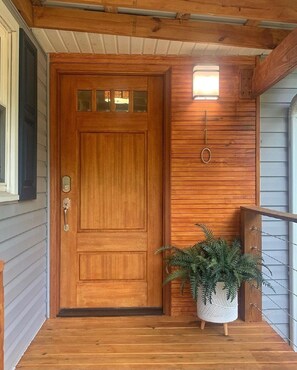Welcome to a charming entrance, featuring a wooden door with a glass panel and a cozy porch with a metal railing.