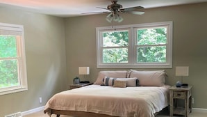 A bedroom with a bed, two bedside tables, a ceiling fan, and a window with a view of trees. - Beautiful lake house perfect for amazing getaways! (Fair Play)