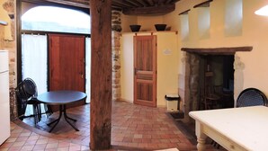 A rustic interior with a stone fireplace, wooden beams, a dining table, and a stone wall. - Gîte for 8 to 10 people in the heart of the Monts d'Ardèche National Park. (Pourchères)