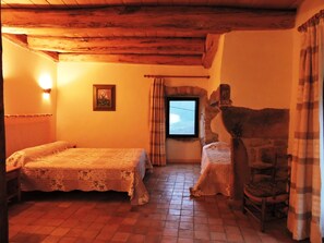 Ein rustikaler Raum mit Holzbalkendecke, einem Bett mit floralem Überwurf, einem Sessel und einer Steinwand.