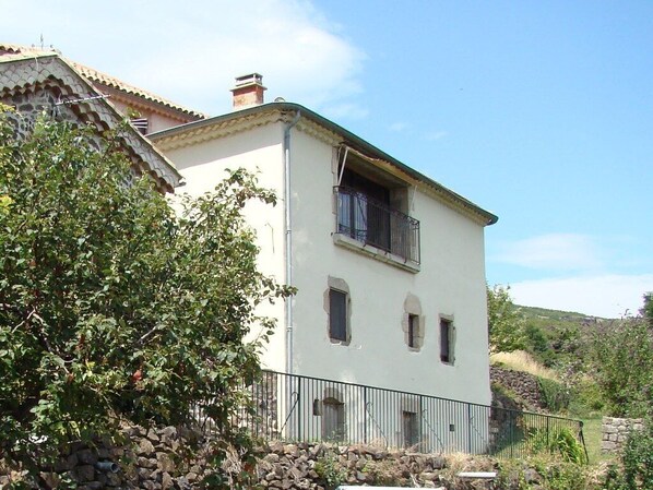 Ein zweistöckiges Gebäude mit weißer Fassade, einem Balkon im zweiten Stock und einer Steinmauer davor.