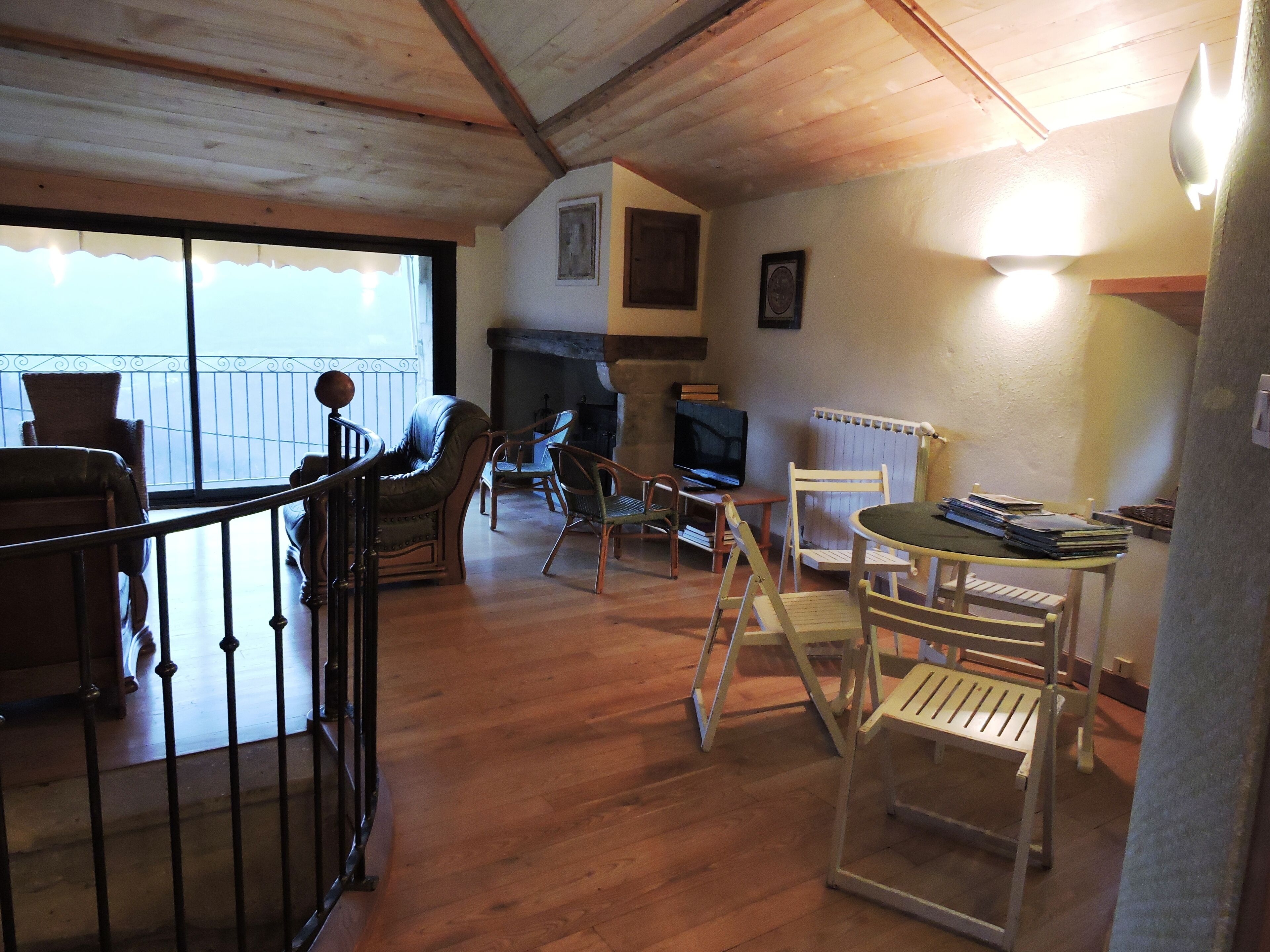 Ein geräumiger Wohnbereich mit Holzboden, Kamin, Fernseher und einem Balkon mit Geländer.