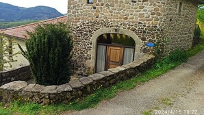 A stone building with a tiled roof, a wooden door, and a stone wall with a sign. - Gîte for 8 to 10 people in the heart of the Monts d'Ardèche National Park. (Pourchères)