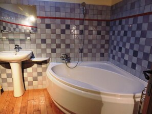 Ein Badezimmer mit einer weißen Badewanne, einem Standwaschbecken und einer Dusche mit Duschhandbrause. Die Wände sind mit einem Schachbrettmuster gefliest.
