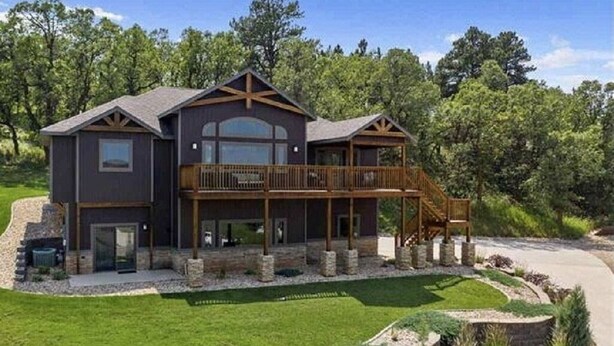 A two-story house with a balcony, a stone foundation, and a landscaped yard. - Spearfish South Dakota rally rental (Spearfish)