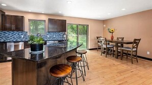 A modern kitchen with a large island, bar stools, and a dining area with wooden chairs and a table. - Spearfish South Dakota rally rental (Spearfish)