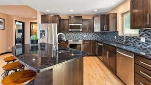 A modern kitchen with dark wood cabinets, stainless steel appliances, and a black granite countertop. - Spearfish South Dakota rally rental (Spearfish)