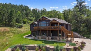 A large, two-story house with a wooden deck and a staircase leading to a second-floor balcony. - Spearfish South Dakota rally rental (Spearfish)