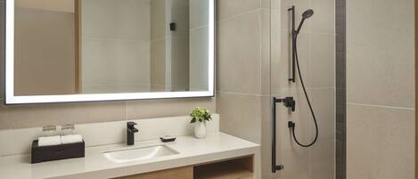 A modern bathroom with a large mirror, a sink, a shower, and neatly folded towels on a shelf.