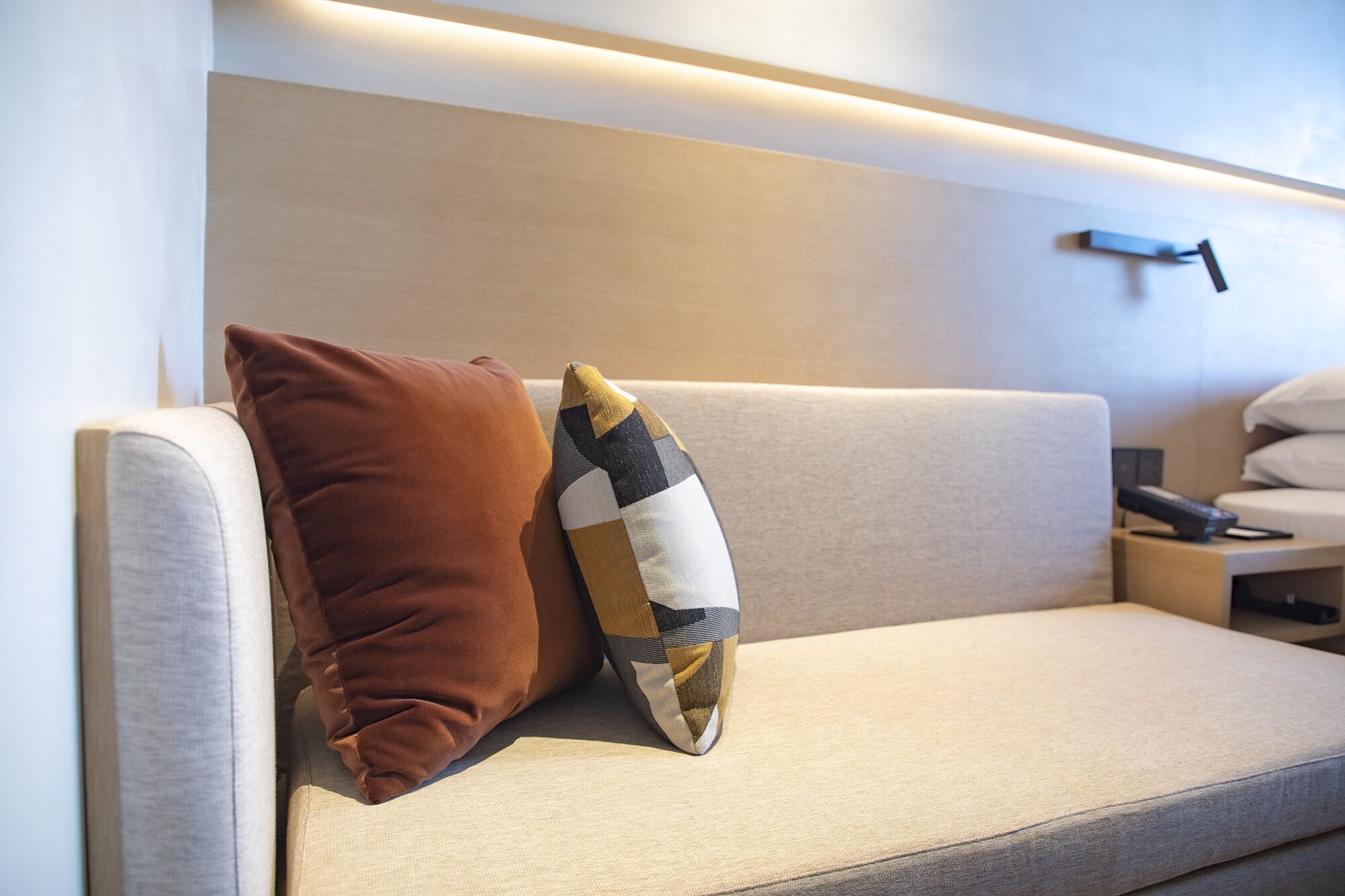Un canapé moderne avec deux coussins, une télécommande et un luminaire fixé au mur.