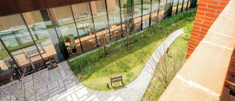 A modern building with large glass windows, a paved courtyard, and a brick wall.